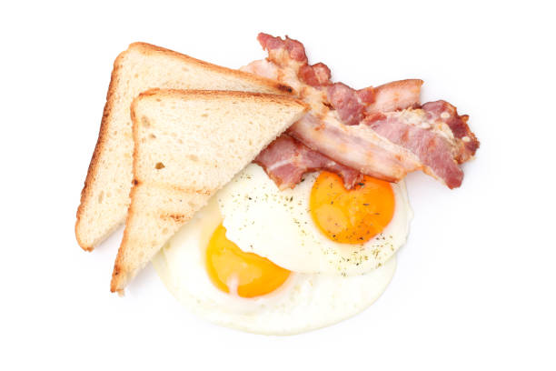 A large plate of delicious and nutritious breakfast on a wooden table, scrambled eggs, fried bacon and toasted bread, cutlery nearby. Close-up.