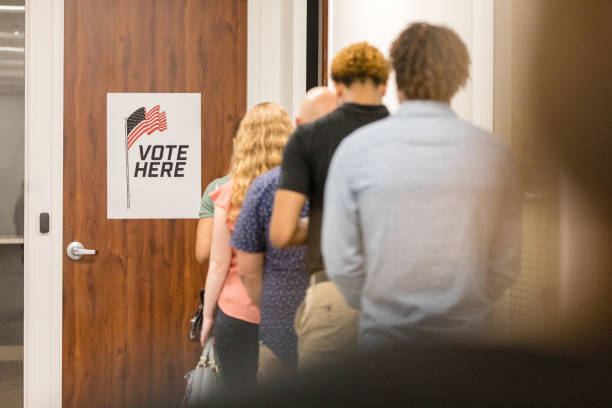 Rear view of long line of unrecognizable diverse voters A rear view of a multiracial group of people standing in a long line in order to vote in the election. teens-in-line stock pictures, royalty-free photos & images