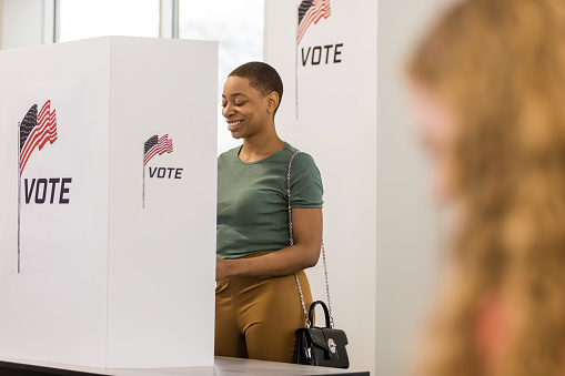 A cheerful young adult woman votes in privacy at the voting booth.