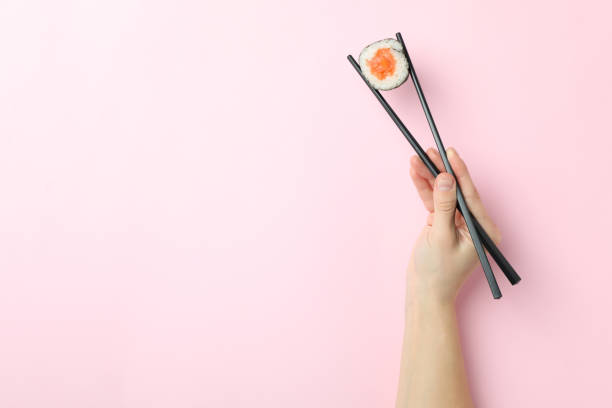 istock Female hand holds sushi with chopsticks on pink background 1495398323