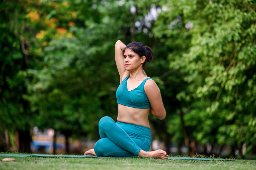Young yogi attractive woman in Cow Face pose or Gomukhasana at park in morning daylight. Concept of yoga and meditation for healthy lifestyle.