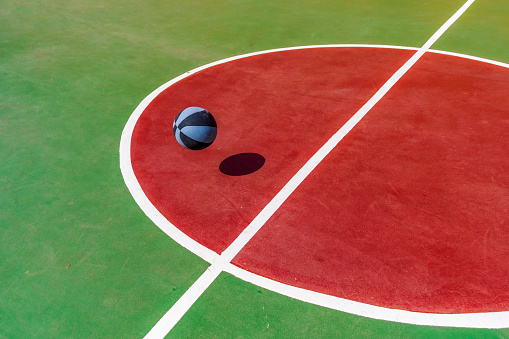 Red and green basketball court with a gray striped ball frozen in full pot with shadow on the ground