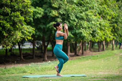 Attractive Young woman wearing sports dress practicing yoga , standing in Eagle pose or Garudasana at park in morning. Concept of of yoga and healthy lifestyle.