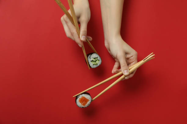 istock Female hands hold chopsticks with maki on red background 1495400613