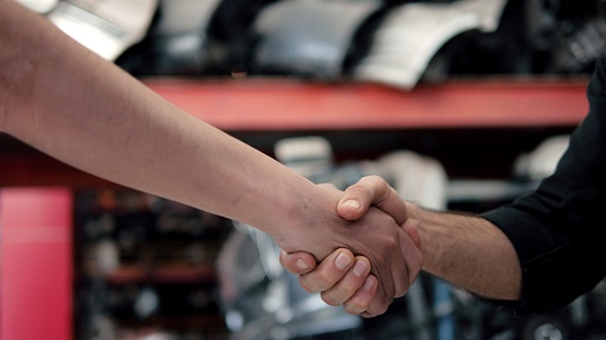 Close up hands of automotive mechanic shaking hands with client at auto repair shop. Car service, repair, maintenance concept