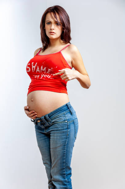 depressed looking pregnant young woman with brown hair in jeans and sleeveless top holding her big belly