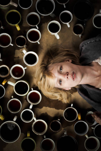 el concepto de una fecha límite, la necesidad de mantenerse alegre. mujer rodeada de muchas tazas de café. - dependency caffeine tired women fotografías e imágenes de stock