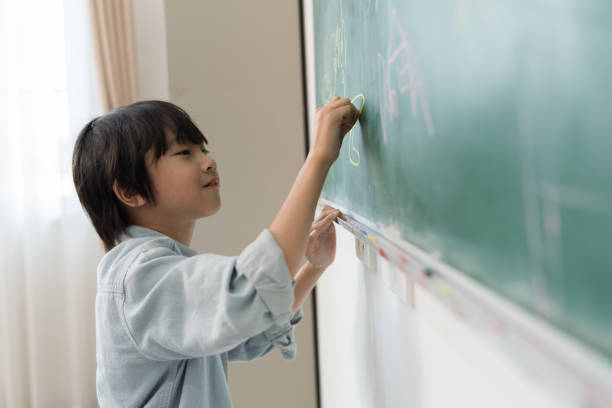 istock Happy boy using chalk writing on board in classroom at school. Student learning in the class. Children and education concept 1495404653