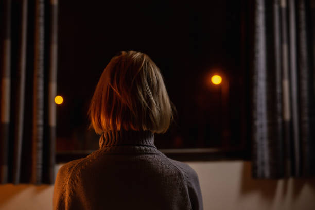An unrecognizable woman sits alone in a dark room. Reflections, depression, heavy thoughts, loneliness concept.