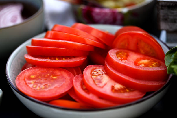 Tasty fresh red tomato slices on a wooden cutting board isolated on light background: Selective focus. Diet and healthy food concept