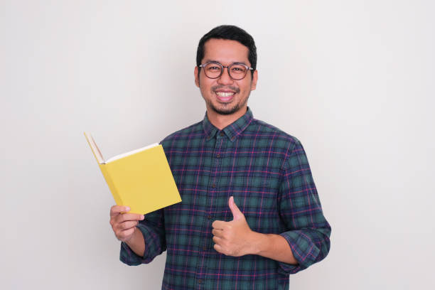 istock Adult Asian man smiling and give thumb up while holding a book 1495411331