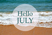 Hello July greeting card with text with on blue ocean water and sandy beach background.Summer vacation,relax or travel concept.