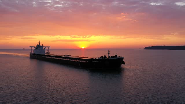 An elegant cargo ship gliding gently under the sun at sunset. A bulk carrier loaded with grains sailing from the open sea towards Bosphorus under a crimson sky