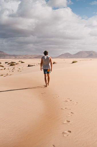 Young man walking calmly on the desert sand of the dunes of Corralejo in Fuerteventura, in summer, during a vacation trip through the Canary Islands