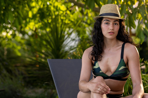 A front view of a  young woman who is enjoying a mindful moment  by the pool she is wearing a trilby hat and is willing on a sun lounger. She is enjoying a nation to Toulouse in the south of France.