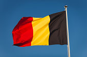 Flag of Belgium on mast. National flag against wind blue sky. Flag of Belgium, capital Bruxelless. National symbol of Kingdom of Belgium