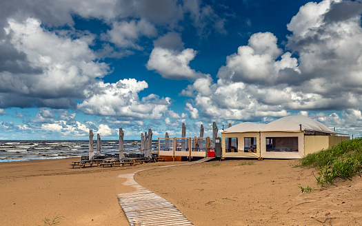 Coastal summer landscape with sandy beach, pedestrian walkway leading to resting deserted area and stormy weather with beautiful cumulus clouds above the Baltic Sea