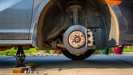 Wheel well of a vehicle lifted with a tire jack. Rusted hub and strut visible. High quality photo