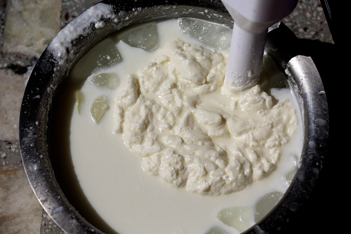 House wife making butter from a milk cream storage by help of hand blender in home close up.