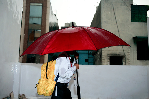 Young handsome man using a airpods while holding a black umbrella while walking in a city on a rainy day