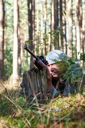 Shooting in the forest from an air rifle with an optical sight. Sunny summer day, front view.
