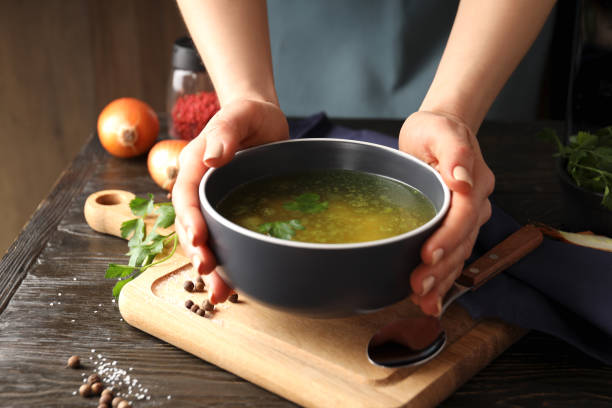 istock Female hands hold chicken soup or broth on a wooden table 1495422367