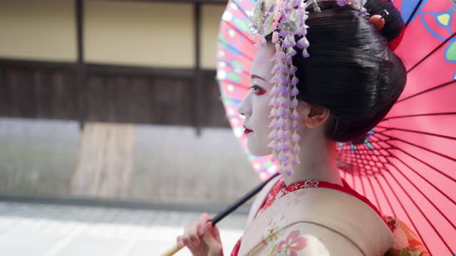 Side view of Japanese Maiko (Geisha in training) walking on street and live streaming in Gion, Kyoto - using Japanese traditional paper umbrella