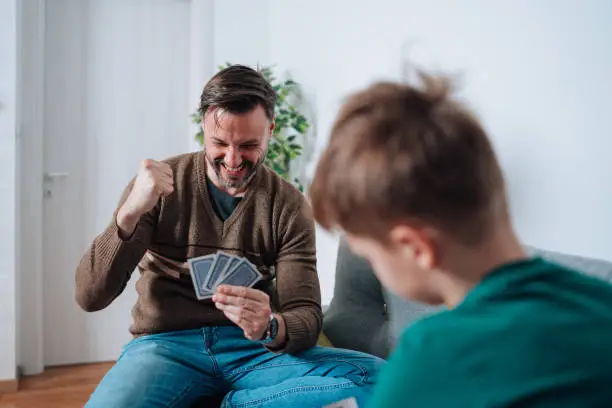 The living room sofa transforms into a playground of friendly competition as the mid adult man and his son engage in strategic battles, their eyes fixed on the board, eager to outwit each other