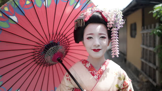 Japanese Maiko (Geisha in training) walking on street and live streaming in Gion, Kyoto - using Japanese traditional paper umbrella