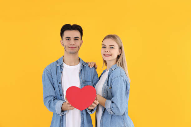 istock Cute couple with heart on yellow background 1495432567