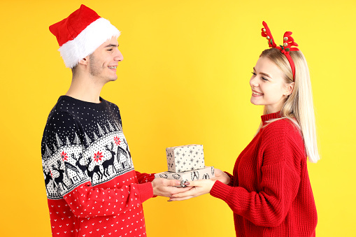 Cute couple in Christmas clothes on yellow background