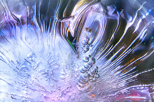 Macro focus-stacked shot of a melting ice cube in a glass of colored liquid, showcasing the beautiful inner structures that can be found within, before they melt and are gone forever.