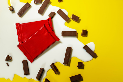 Tow blank red packaging of a chocolate wafers in the puddle of spilled milk. And broken chocolate wafers around. Isolated on yellow background