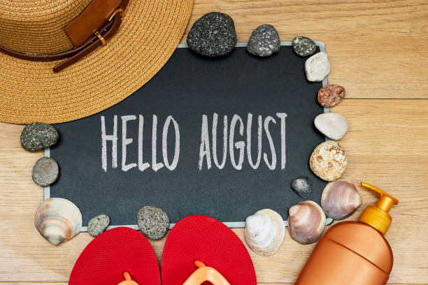 istock summer concept, sun cream and slipper with hello August text on chalkboard and stones. seashell hat on wood table 1495444488