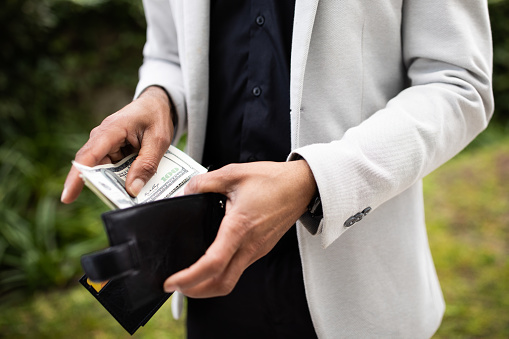 Unrecognizable black man taking out dollar cash money from wallet outdoors, businessman pulling usd money banknotes, counting finances, cropped, closeup
