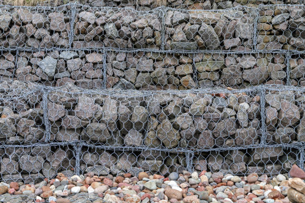 Bank stabilization and protection. Gabion dam surface as a background. Stones in wire mesh structure Bank stabilization and protection. Closeup of a gabion dam surface as a background. Stones of different shapes and sizes in wire mesh structure erosion control stock pictures, royalty-free photos & images