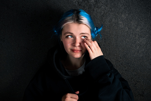 Portrait of a sad woman in a black hoodies with blue hair on a dark background