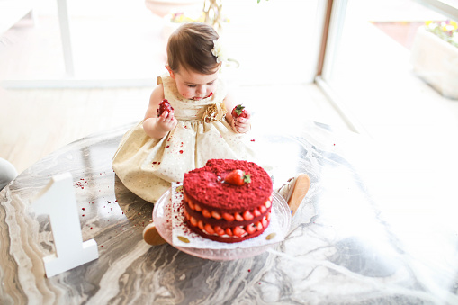 Little girl celebrating her 1st birthday distributes her cake