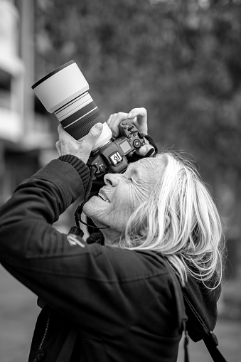 Black and white senior woman taking photos with DSLR camera, background with copy space, full frame vertical composition