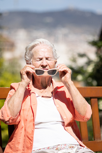 white-haired elderly caucasian woman putting on her sunglasses on a hot sunny summer day. concept of heat wave and uv ray protection.vertical image.