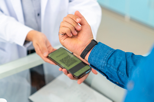 Medical pharmacy and contactless payment concept. Asian man patient customer using smart watch scan QR code on counter making online banking payment buying medicine, drugs and supplement in drugstore