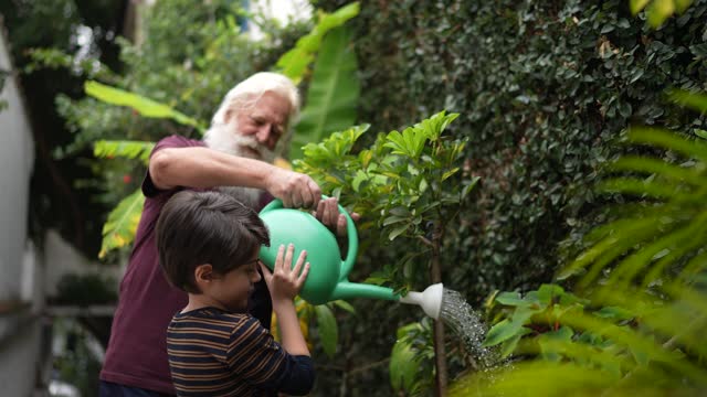 Grandfather and grandson watering plants at home