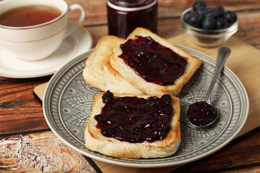 Delicious toasts with blueberry jam and cup of tea on wooden table