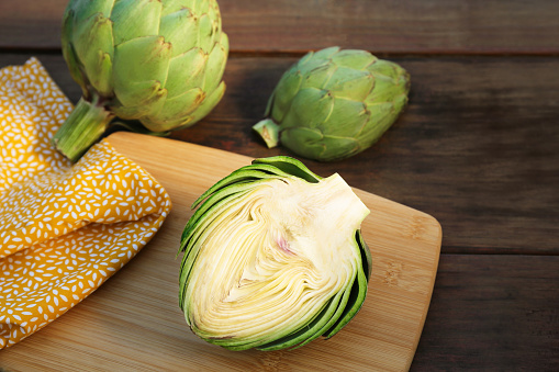 Whole and cut fresh raw artichokes on wooden table, closeup