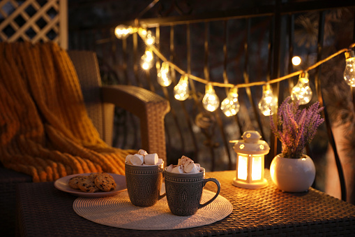 Cups with tasty cocoa and marshmallows on rattan table at balcony in evening