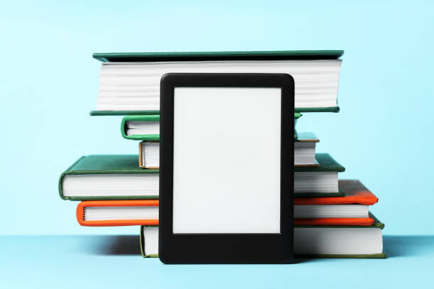 istock Modern e-book reader and stack of hard cover books on light blue background 1495506465