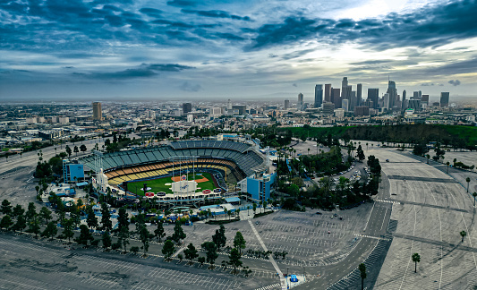 As if suspended in a tranquil moment of time, Dodger Stadium rests in its empty grandeur, awaiting the energetic thrum of fans yet to fill its stands. In the background, the skyline of downtown Los Angeles rises with its architectural variety, beautifully crisp after a cleansing rain has swept away the usual cloak of smog. Above, a sky of perfect clarity arches, imbuing the scene with an airy brightness that seems to lend the stadium and the city beyond an ethereal quality. It's a quiet testament to the city's resilience and the enduring allure of America's favorite pastime.