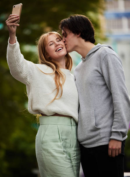 Couple take selfie, man kiss woman with happiness outdoor, social media content and memory with love and relationship. Commitment, partnership and trust with travel, smile in picture and gen z people la pareja se toma una selfie, el hombre besa a la mujer con felicidad al aire libre, el contenido de las redes sociales y la memoria con el amor y la relación. compromiso, asociación y confianza con los viajes, la sonrisa en la imagen y las personas de l