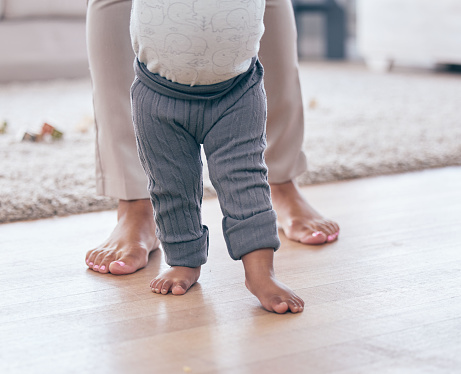 Baby feet, walking and learning with mother in a living room lounge with mobility development. Floor, home and first steps of a young kid with mama together with love, care and support in a house