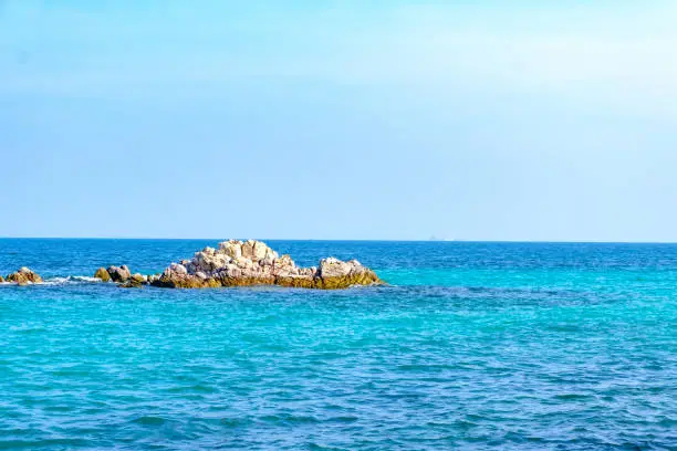 A rock formation in the middle of the sea surrounded by bright blue water.Sea scape